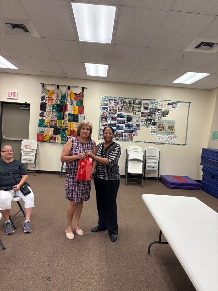 Two woman smile for a photo, holding a gift bag.